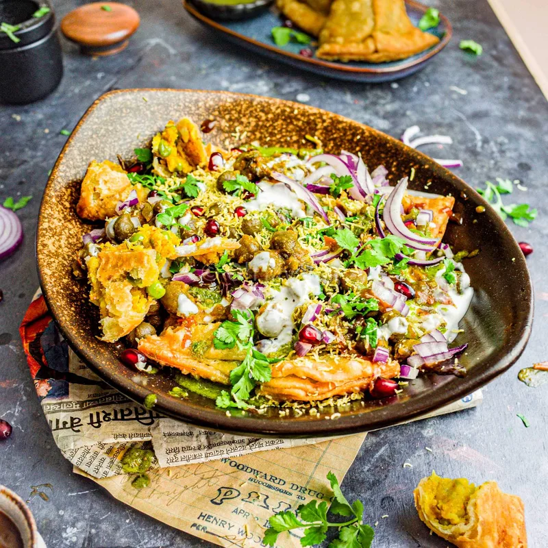 Crushed samosas topped with yogurt, chutneys, and spices